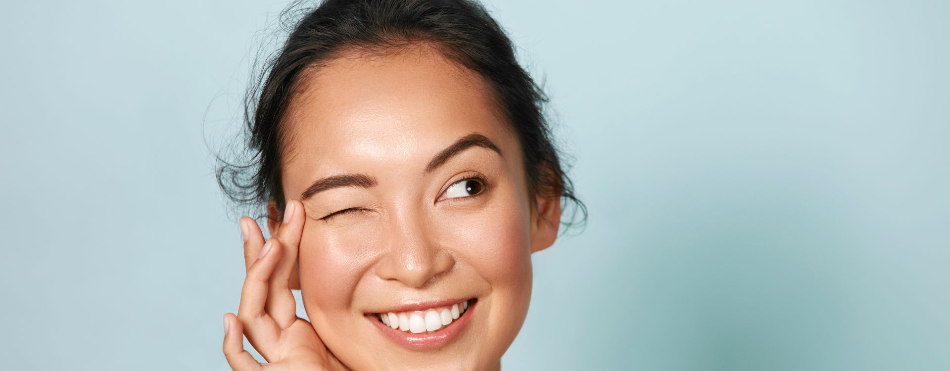 STEINKRAFT Zeolith für Menschen Kosmetik - am Bild zwinkert eine Frau mit braunen Haaren und vitaler Haut